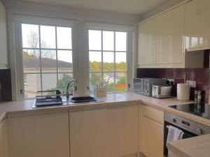 una cocina con armarios blancos, fregadero y ventanas en Spacious 2-bed with Free Parking, en Inverness
