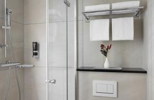 a bathroom with a shower with towels and a vase of flowers at Leonardo Hotel Nürnberg in Nuremberg