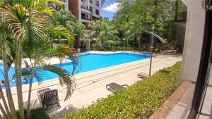 a swimming pool in front of a building with palm trees at Amplio departamento en Asunción in Asunción