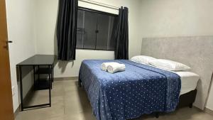 a bedroom with a bed with a blue blanket and a table at Apartamento mobiliado com Wi-Fi in Sinop
