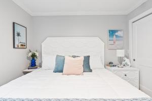 a white bedroom with a large white bed with blue pillows at 100 Steps to beach access - 5 minute walk to the Village - Private Porch in Siesta Key