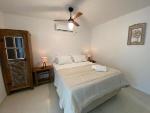 a white bedroom with a bed and a ceiling fan at Paraíso Geribá in Búzios
