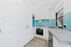 cocina con armarios blancos y paredes azules en Mooloomba Four by Discover Stradbroke, en Point Lookout