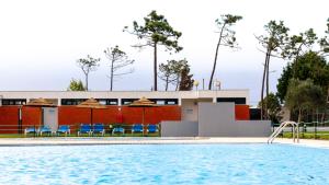 a swimming pool with chairs and a building at Parque De Campismo Orbitur Gala in Figueira da Foz