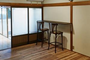 a table and two stools in a room with windows at ふもとの山小屋 ネイバーズ Neighbors - Alpine Base Inn in Matsumoto