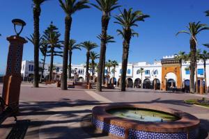 a fountain in a plaza with palm trees and a building at Dar lara in Larache