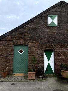 a brick building with green doors and two windows at Kunst & Wohnen auf dem Bauernhof in Krefeld