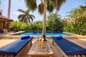 a pool with two blue cushioned benches next to a palm tree at Baan Buaa - Beachside 3 Bed Pool Villa in Hua Thanon Beach