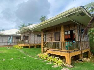 a house with a porch and a green yard at Villa Malinao Oceanview Resort- Superior Bungalow in Burgos