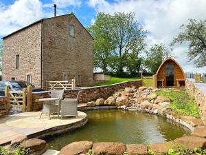 un edificio in pietra con un laghetto di fronte di Owls Nook Barn, Luxury Barn with Hot Tub & Sauna a Sandford