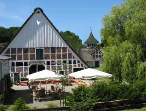 ein Gebäude mit Tischen und weißen Sonnenschirmen davor in der Unterkunft Taubenhof - Gut Cadenberge in Cadenberge