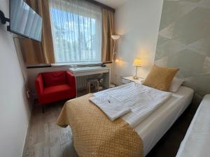 a bedroom with a bed with a red chair and a window at Hotel Gloria Budapest City Center in Budapest