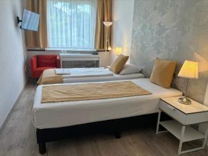 a bedroom with two beds with a red chair and a window at Hotel Gloria Budapest City Center in Budapest