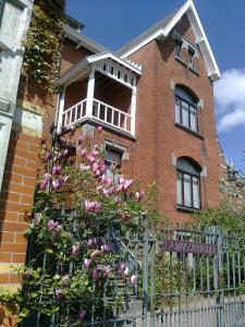 een stenen huis met een hek en roze bloemen bij La Maison Brodée in Écaussinnes-dʼEnghien
