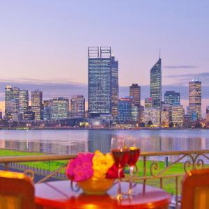 stolik z dwoma kieliszkami wina i panoramą miasta w obiekcie The Peninsula Riverside Serviced Apartments w mieście Perth