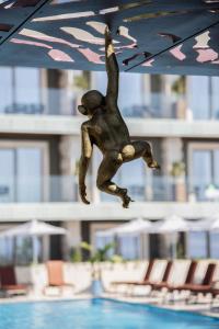 a statue of a monkey hanging from a umbrella over a swimming pool at Hotel Vlora Priam, Affiliated by Melia in Vlorë
