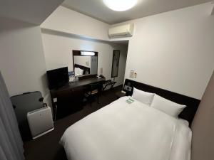 a hotel room with a white bed and a desk at Hotel Route-Inn Uozu in Uozu