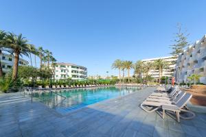 a pool with lounge chairs and palm trees and buildings at Ura Hotels Jardín Del Atlántico in Playa del Ingles