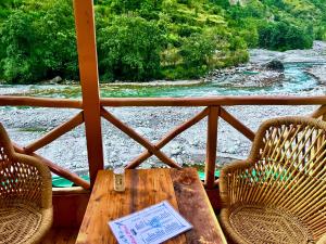 un tavolo e sedie su un portico con un fiume di Hotel Himalayan Valley View Retreat - Best Selling Riverside Hotel in Manali a Manāli