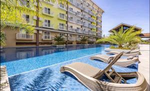 a swimming pool with lounge chairs next to a building at Mactan Cozy Hub Amani Grand in Lapu Lapu City