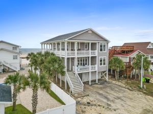 a house on the beach with palm trees at Experience luxury at On The Rocks, spacious 4 bedroom retreat with private pool! in Ocean Isle Beach