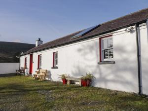 a white building with red windows and a table and benches at Dan White's Cottage in Newry