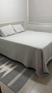a bedroom with a bed with white sheets and a rug at Apartamento Cabo Frio Praia do Forte in Cabo Frio