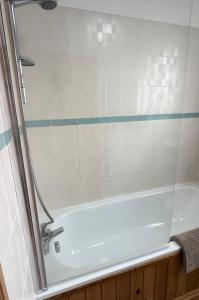 a white bath tub with a glass shower door at Wheel Corner Cottage in Kingsteignton