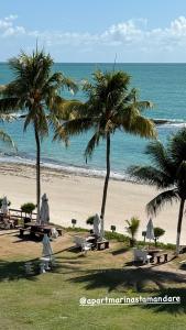 a beach with palm trees and picnic tables and the ocean at Apart Hotel Marinas Tamandaré in Tamandaré