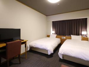 a hotel room with two beds and a desk and a television at Dormy Inn PREMIUM Kushiro in Kushiro