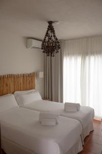 two white beds in a bedroom with a chandelier at Hostal La Torre Ibiza Cap Negret in San Antonio