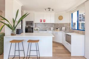 a kitchen with white cabinets and bar stools at Heritage 301 in Tuncurry