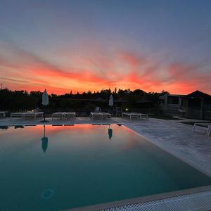 a sunset over a swimming pool with tables and benches at Agriturismo & Agricamping Serena in Pastrengo