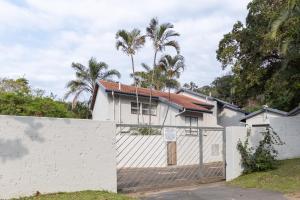 a white house with a fence and palm trees at Unit 4 Springvale in Zinkwazi Beach