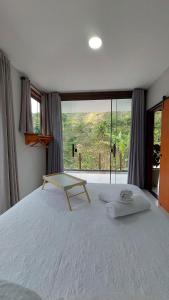 a bedroom with a white bed with a large window at Casa da Bella - 1,5km do centro de Lumiar in Nova Friburgo