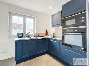 een grote keuken met blauwe kasten en een raam bij La Marée - Appt à 50m de la plage in Bray-Dunes