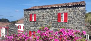 a stone building with red windows and pink flowers at Casal do Vulcão in Capelo