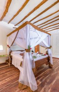 une chambre avec un lit à baldaquin avec des rideaux blancs dans l'établissement Hakuna Majiwe Beach Lodge, à Paje