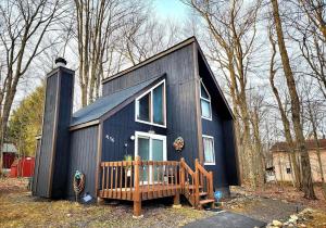 a black tiny house in the woods with a porch at Cozy Ski Chalet in the Heart of the Poconos in Tobyhanna