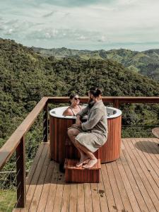 un hombre y una mujer sentados en una bañera en una terraza en Cabana na montanha com Ofurô ao ar livre, churrasqueira, trilha com cascata e Starlink, en Cambuí