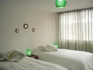 キトにあるCasa San Juan Quitoのベッドルーム1室(ベッド2台付)、緑色の照明付きの窓が備わります。