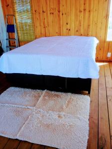 a bedroom with a bed with white sheets and a rug at 28 de Octubre in Punta Del Diablo