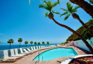 a swimming pool with palm trees and the ocean at Cliffside Villa W Ocean Views & Balcony in Avalon