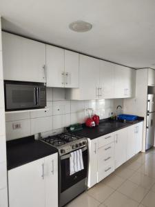 a kitchen with white cabinets and a stove and a microwave at Depa Bonito en Condominio ! in Tacna