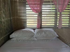a bed with pillows and a window with pink curtains at MALAIKA RESORT in San Vicente