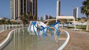 a park with blue chairs in a pool with buildings at SUNSET WAVES sea & sky apartment in Benidorm