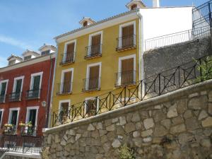 a yellow building with balconies and a stone wall at Alojamientos Turísticos Casco Antiguo in Cuenca
