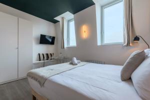 a bedroom with a large white bed with two windows at Studio équipé côté rue, parking gratuit in Villeneuve d'Ascq