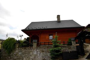 a wooden house with a stone wall in front of it at Alpejskie Domy Ski House in Krynica Zdrój