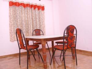 a wooden table with two chairs and a table and a curtain at Royal Residency Apartment in Mundakāyam